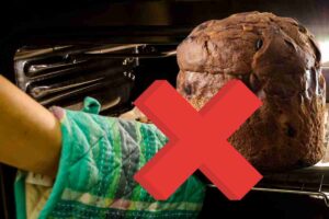 Panettone con forno sullo sfondo, una croce rossa ed una mano con guanto da forno